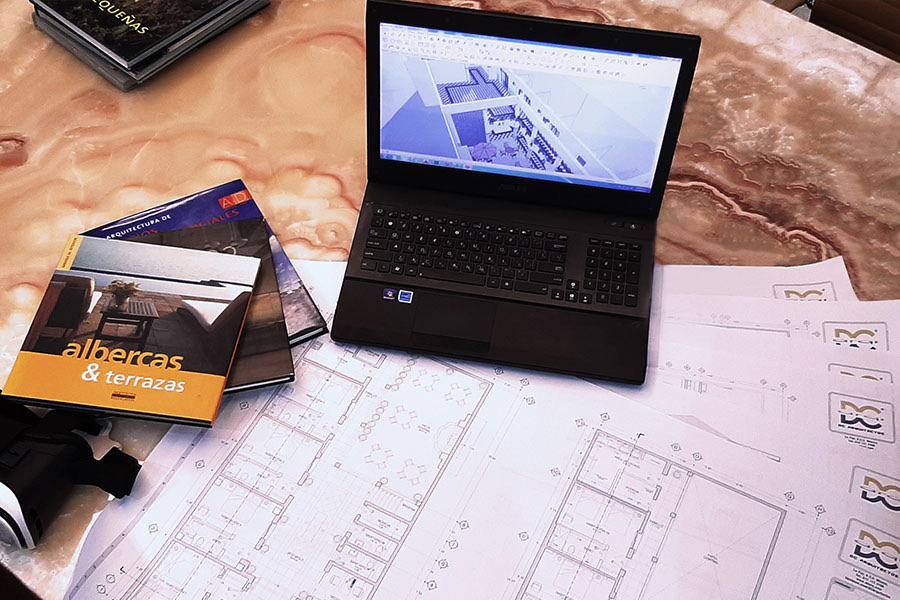 Planos técnicos, portátil con modelo 3D y material de consulta en mesa de trabajo
